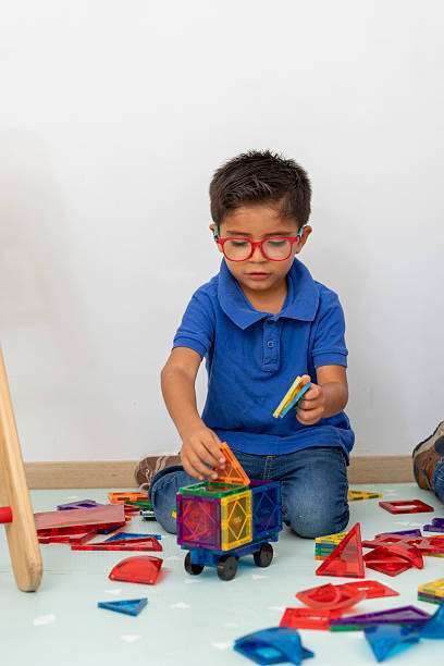 Young hispanic boy with glasses concentrating on building with colorful magnetic tiles at the pediatrician's office