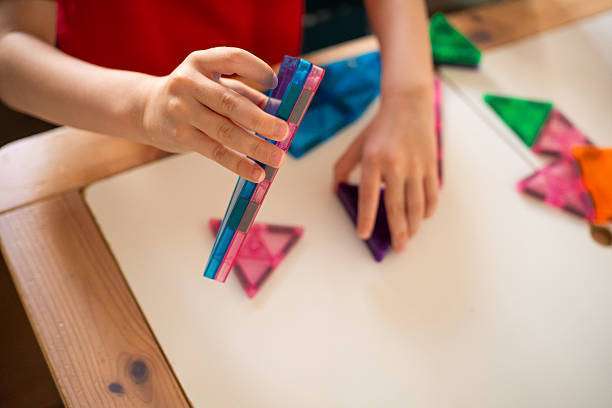 child skillfully assembles colorful magnetic tiles