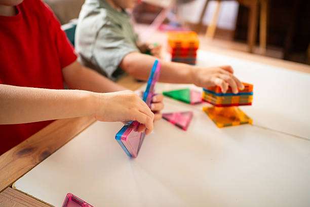 Two children are focused on a creative building activity using colorful magnetic tiles.