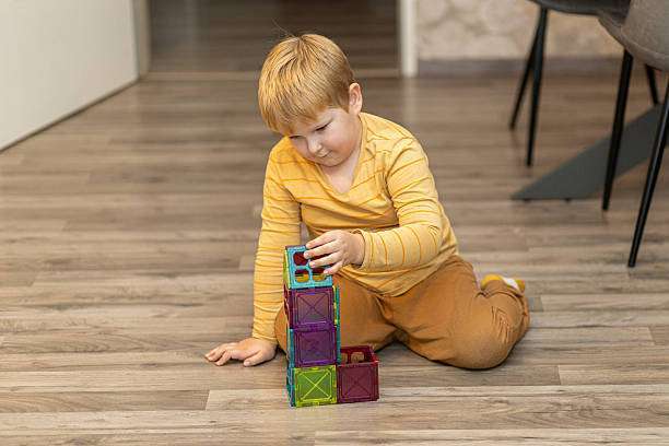 A young boy sits on the floor, focused on stacking vibrant magnetic tiles.