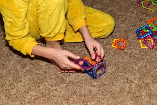 A young boy sits on the floor, focused on stacking vibrant magnetic tiles.