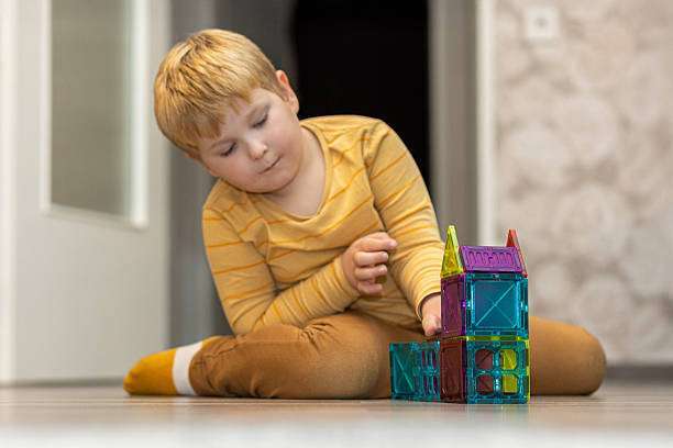 A young boy sits on the floor, focused on stacking vibrant magnetic tiles.