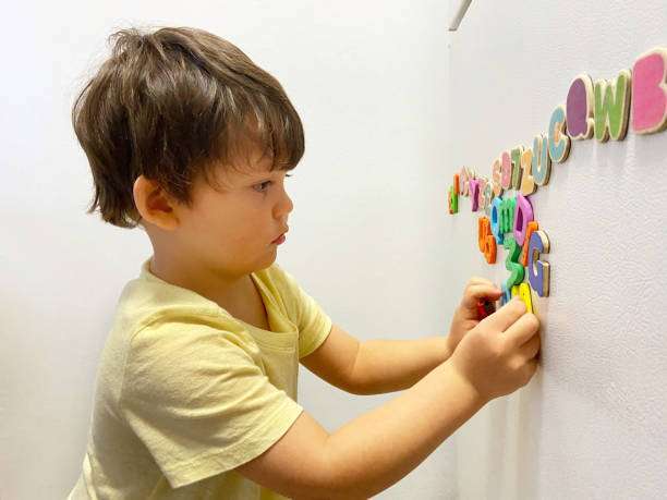View of toddler playing with magnet letters text on refrigerator.magnetic tiles