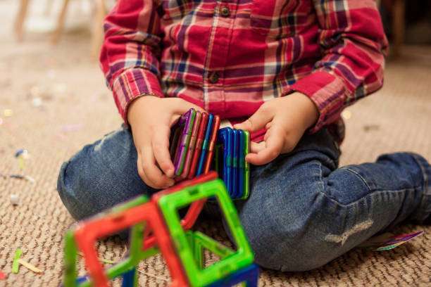 A boy plays with magnetic tiles constructor in a children's room, sitting on cork floor