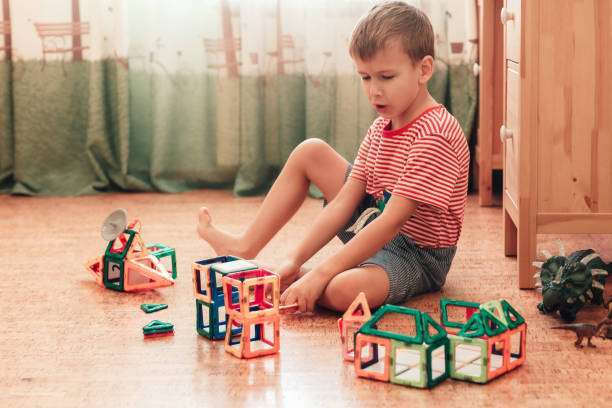 A boy plays with magnetic tiles constructor in a children's room, sitting on cork floor