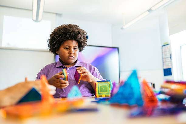 Teacher and diverse elementary students solving logic tasks with different shapes magnetic tiles